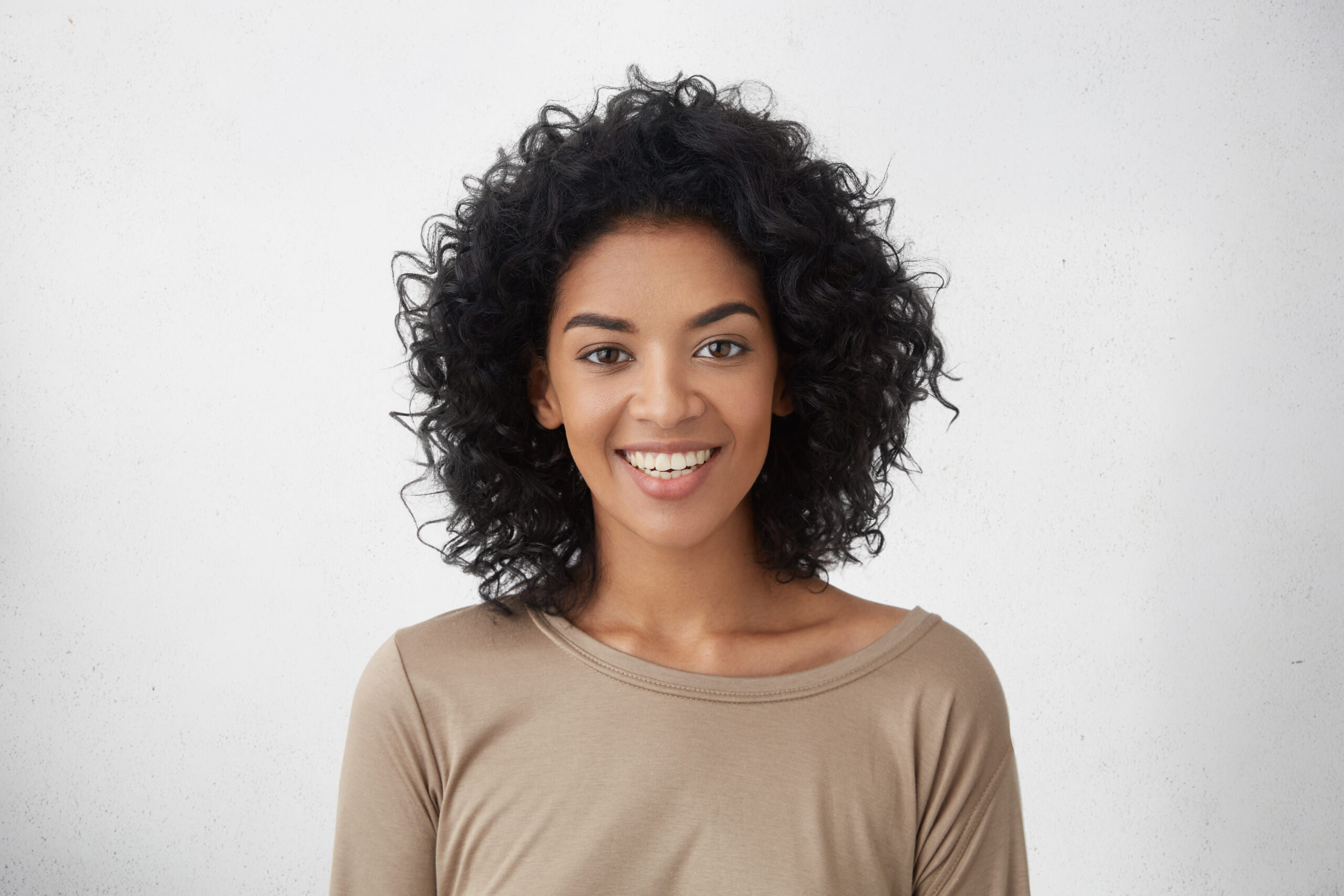 Cheerful dark-skinned girl smiling broadly, rejoicing at her victory in competition among young writers, standing isolated against grey wall background. People, success, youth and happiness concept